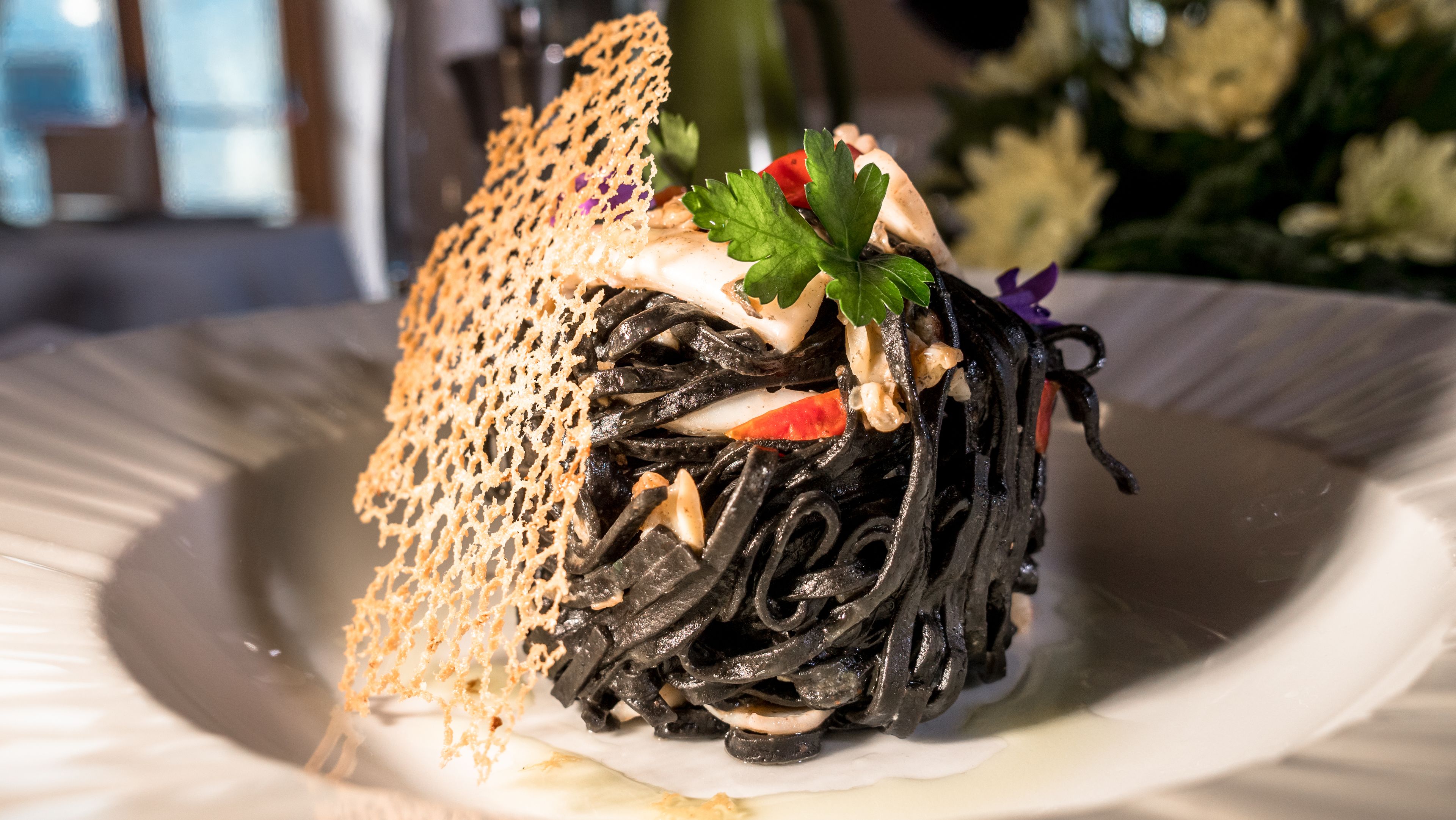 A dish with black noodles, vegetables, and a decorative leaf garnish on a white plate.