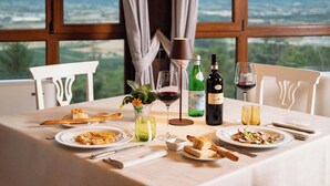 A dining table set with plates of food, wine glasses, and bottles, with a scenic view through the window. - Borgo di Celle (Città di Castello)