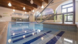 A swimming pool with clear lane markings, a wooden ceiling, and a view of a cityscape through large windows. - Borgo di Celle (Città di Castello)