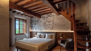A bedroom with a large bed, a wooden staircase, a chair, and a patterned wall. - Borgo di Celle (Città di Castello)