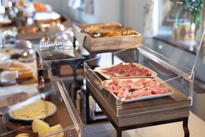 Un bufé con una variedad de alimentos, incluyendo carnes y quesos en porciones.