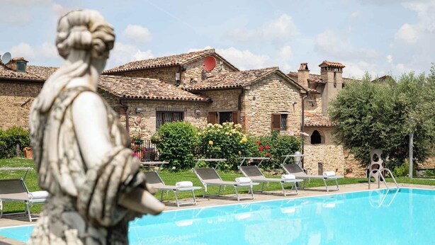 A stone building with a pool, lounge chairs, and a statue. - Borgo di Celle (Città di Castello)