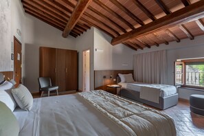 Una habitación de hotel con techo de madera, dos camas, una silla, una mesita de noche y una ventana con cortinas.