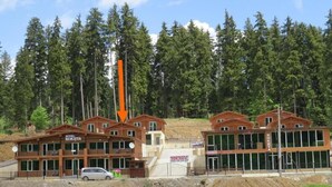 Un hotel con varias cabañas de madera, un letrero que dice "HOTEL KOKHTA" y una obra en construcción al fondo.