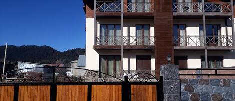 A multi-story building with balconies, a wooden gate, and a stone wall.
