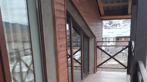 Un pasillo con paredes de madera y grandes puertas de vidrio que dan a un espacio exterior con vistas a edificios y una valla metálica.