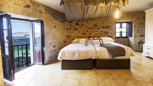 A bedroom with a stone wall, a bed with a headboard, a window, and a balcony.