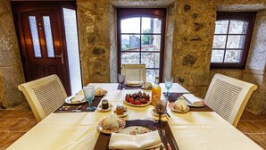 A dining table set for four with a stone wall backdrop, two windows, and a door.