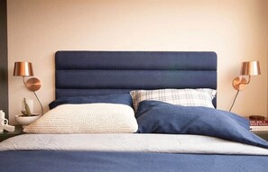A bed with a dark blue headboard, two bedside lamps, and a variety of pillows. - Apartamento em Santo Amaro (São Paulo)