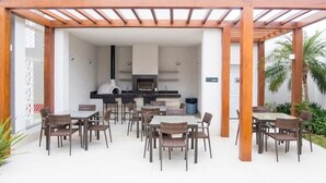An outdoor patio with a wooden pergola, a kitchen area, and multiple dining tables and chairs. - Apartamento em Santo Amaro (São Paulo)