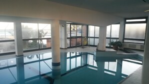 An indoor swimming pool with clear glass walls, large windows, and a tiled floor. - Residence Stella Maris (Pietra Ligure)