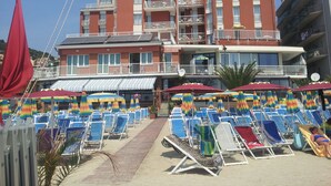 A beachfront hotel with multiple balconies, a pool area with sun loungers, and a clear sky. - Residence Stella Maris (Pietra Ligure)