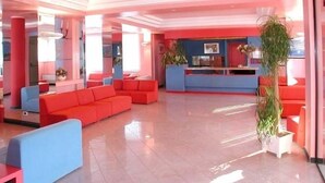 A modern lobby with red and blue seating, a reception desk, and a large potted plant. - Residence Stella Maris (Pietra Ligure)