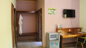 Une pièce avec un bureau en bois, un téléviseur fixé au mur, un petit réfrigérateur et une porte en bois donnant sur une autre pièce.