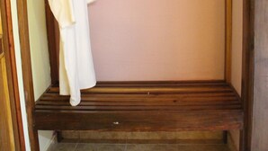 Un banc en bois sur lequel est drapé un vêtement blanc, le tout adossé à un mur uni.