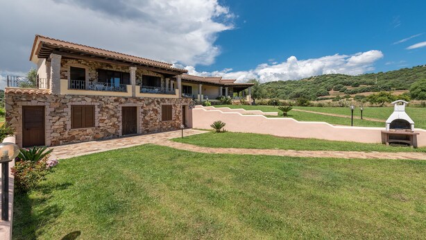 A two-story stone house with a balcony, a stone staircase, and a grassy yard. - AffittaSardegna - Casa Pompia 1 (Siniscola)