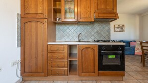 A kitchen with wooden cabinets, a stove, and a sink. - AffittaSardegna - Casa Pompia 1 (Siniscola)