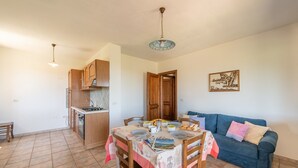 A compact living space with a dining area, kitchenette, and a blue sofa. - AffittaSardegna - Casa Pompia 1 (Siniscola)