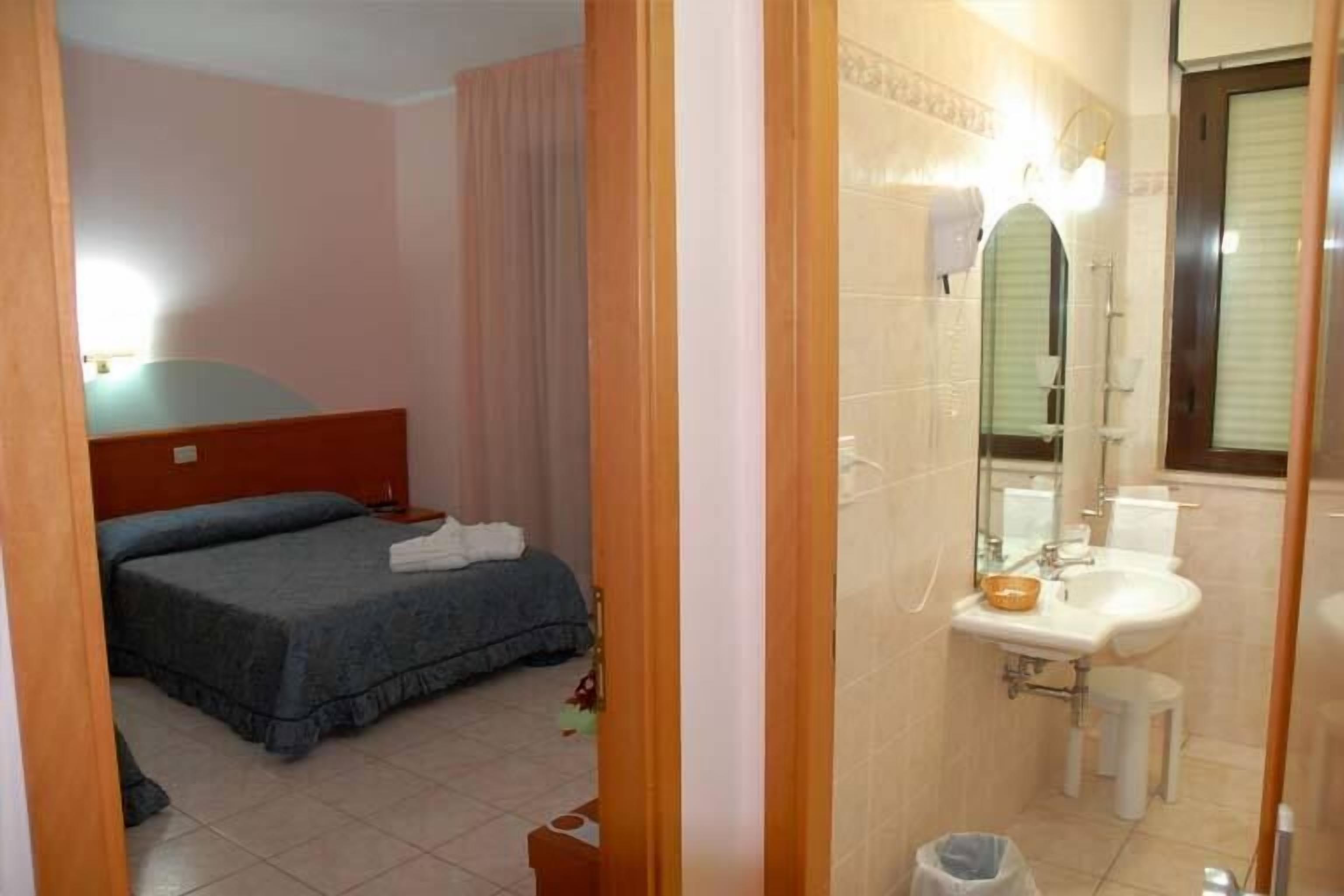 A hotel room with a bed, a bathroom with a sink and mirror, and a door leading to another room.