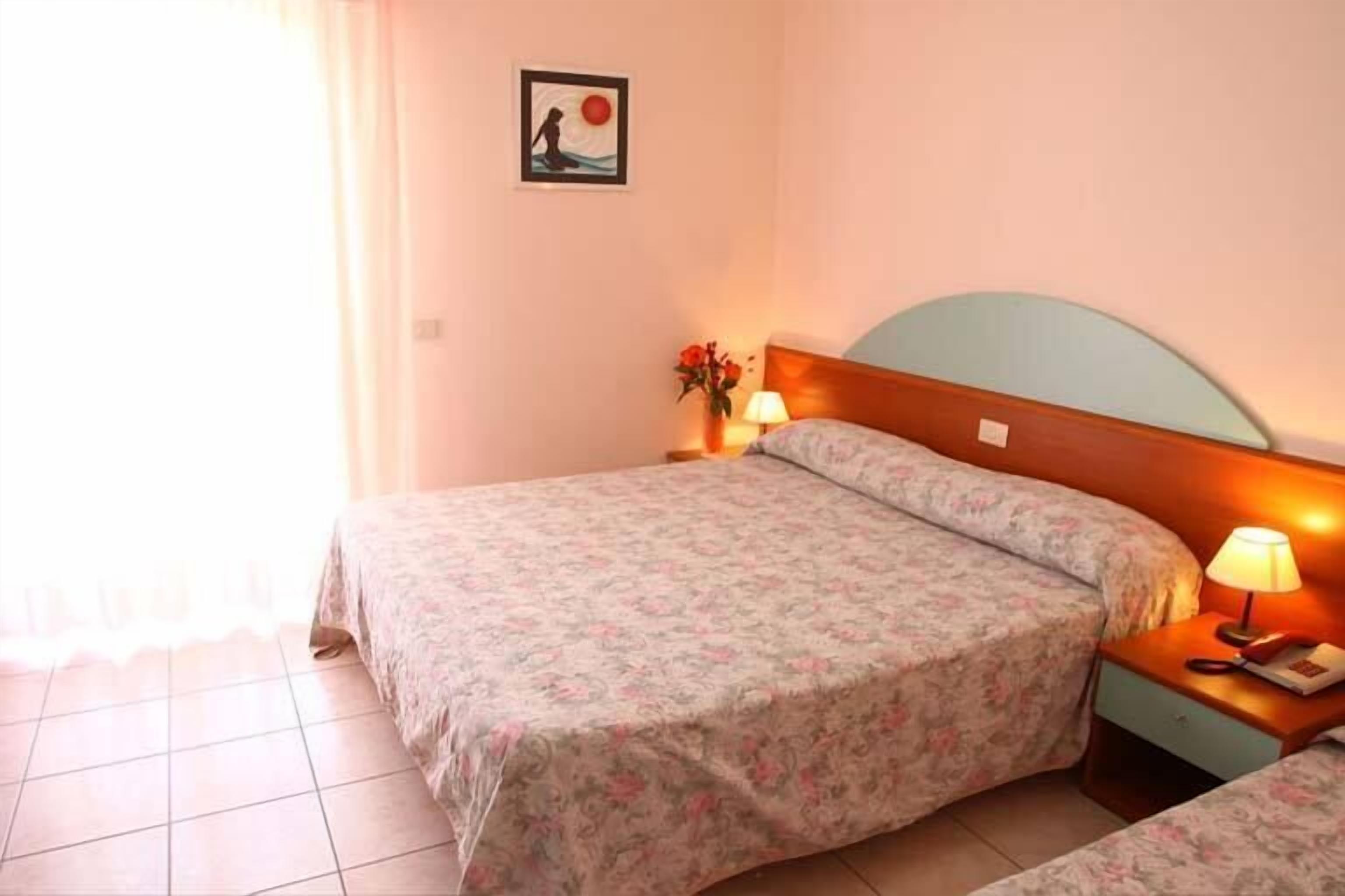 Quarto de hotel com cama, mesa de cabeceira com abajur e quadro na parede.