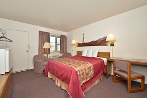 A hotel room with a bed, a desk, two chairs, a wardrobe, and a window with curtains.