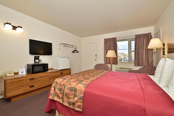 A hotel room with a bed, a television, a desk with a microwave, a telephone, and a window with curtains.