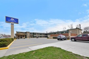 A hotel with a sign indicating it is a Best Value Inn, a parking lot with several cars, and a building with a brick facade.