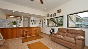 A modern living room with a leather sofa, a kitchen area with a bar, and a large window with a view of a building. - Americas Best Value Inn (North Platte)