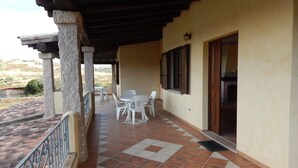 A covered outdoor patio with a tiled floor, white plastic chairs, and a table. - AffittaSardegna - Casa Pompia 6 (Siniscola)