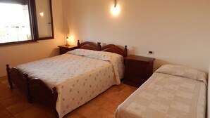 A bedroom with two beds, a nightstand, a bedside lamp, and a wall-mounted light fixture. - AffittaSardegna - Casa Pompia 6 (Siniscola)