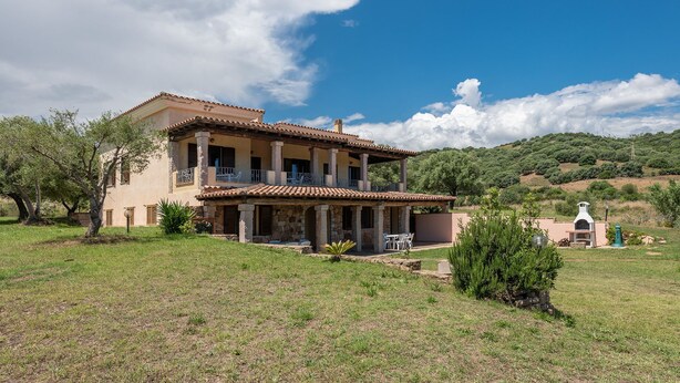 A two-story house with a patio, stone columns, and a view of the surrounding hills. - AffittaSardegna - Casa Pompia 6 (Siniscola)