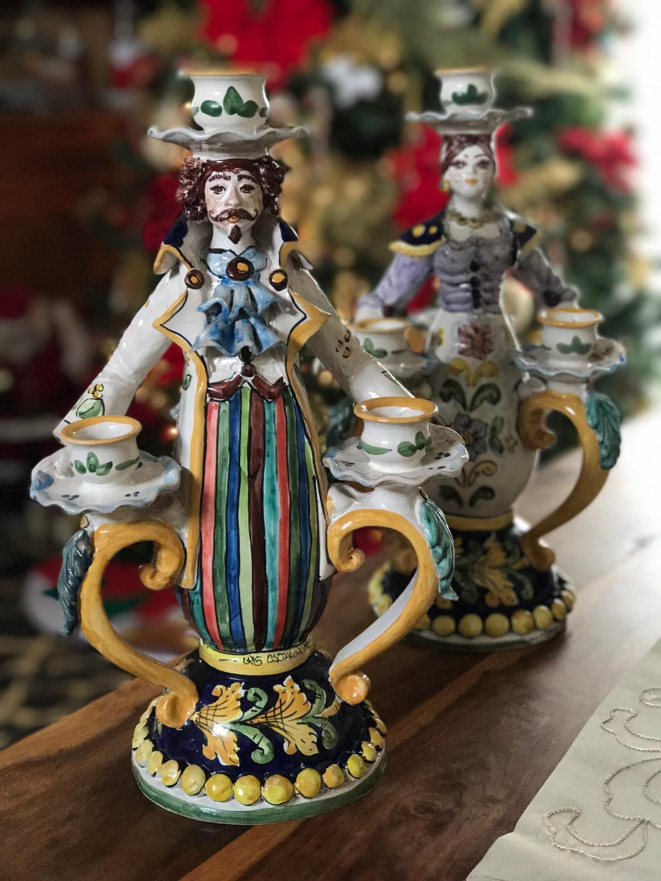 Dos figuritas de cerámica ornamentadas con vestimenta y accesorios detallados, sobre una superficie de madera.