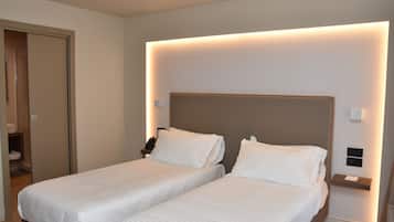 Habitación de hotel con dos camas individuales, una mesita de noche con lámpara y una lámpara de pared.