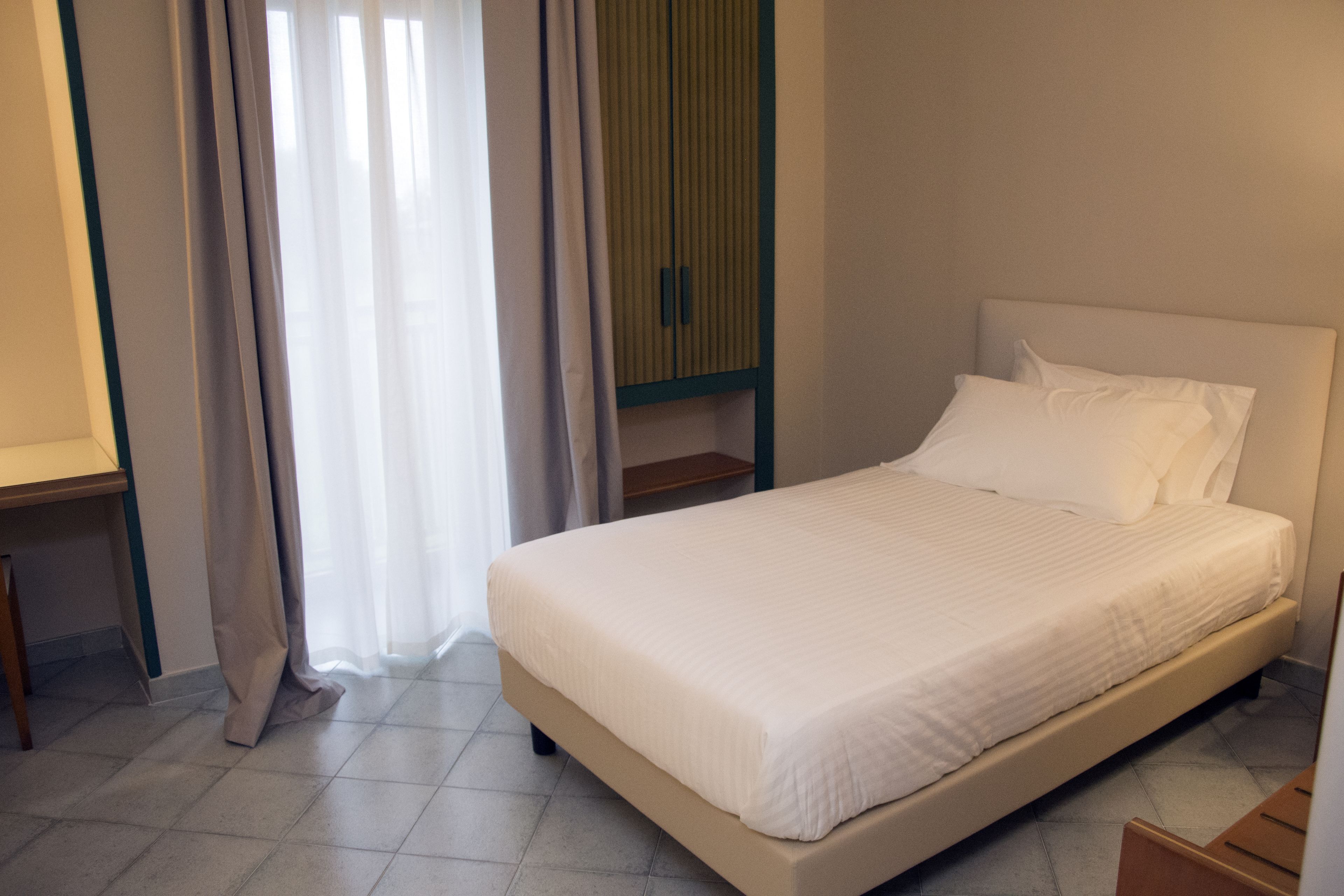 Una cama bien hecha en una habitación con una mesita de noche de madera, una pequeña mesa y un armario.