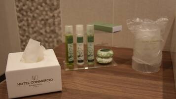 A hotel room with a tissue box labeled "Hotel Comercio Business Hotel" and a set of toiletries on a wooden surface.