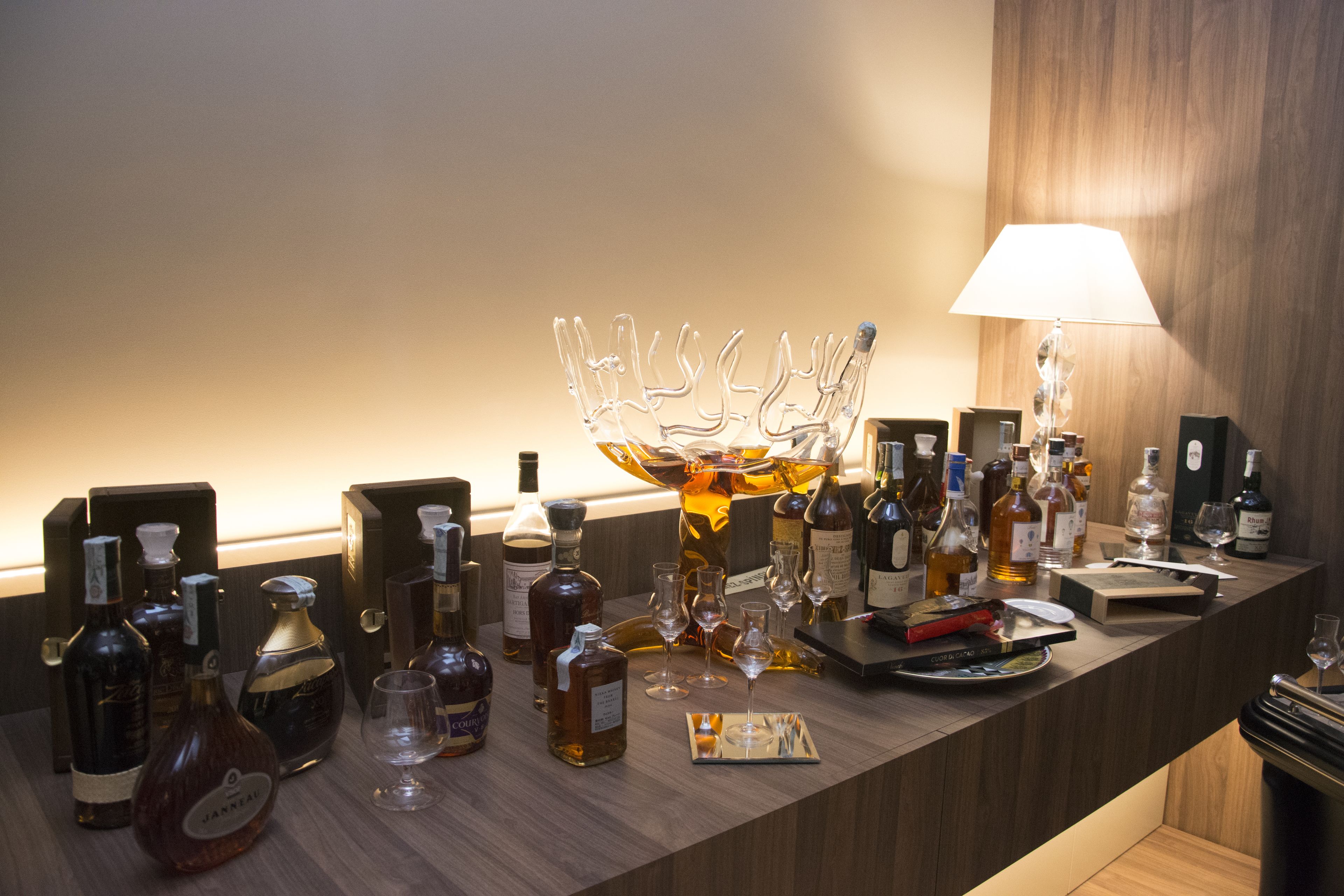 A bar area with various bottles and glasses, a decorative glass piece, and a lamp.