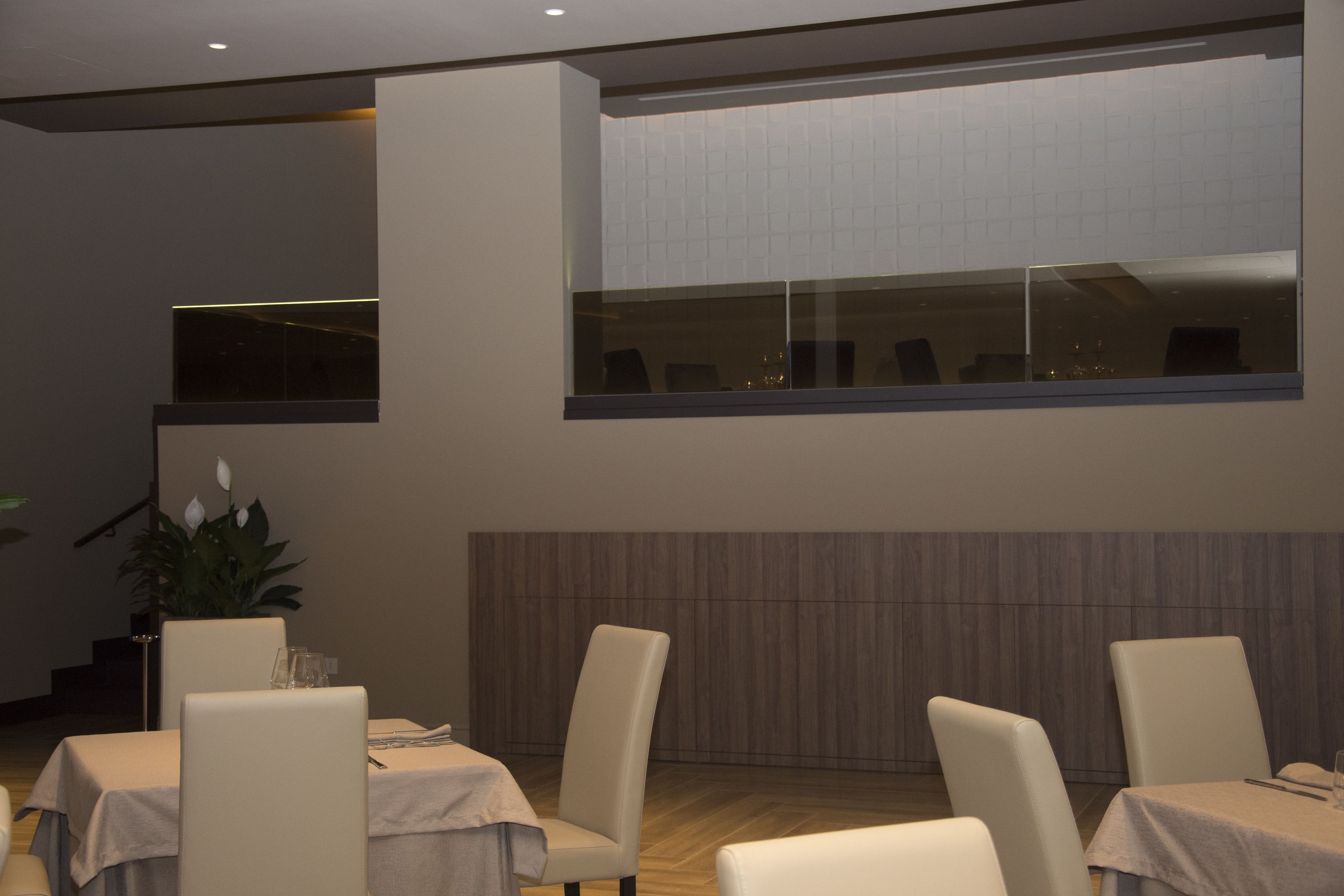 A dining area with tables and chairs, a large window, and a plant.