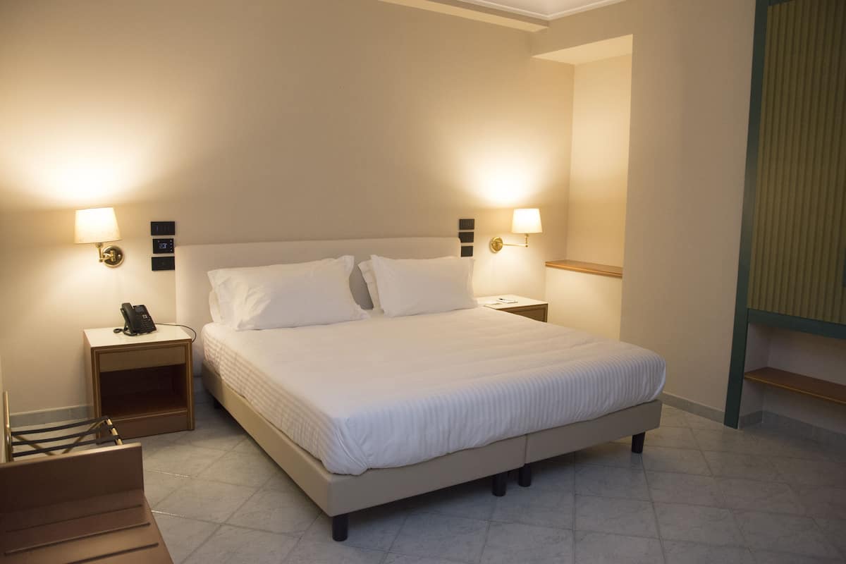 A neatly made bed with white linens, two bedside tables with lamps, and a small wooden nightstand with a phone.