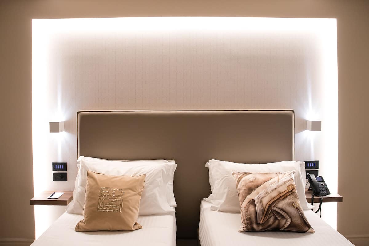 A hotel room with two beds, each with a pillow and a bedside table with a phone.