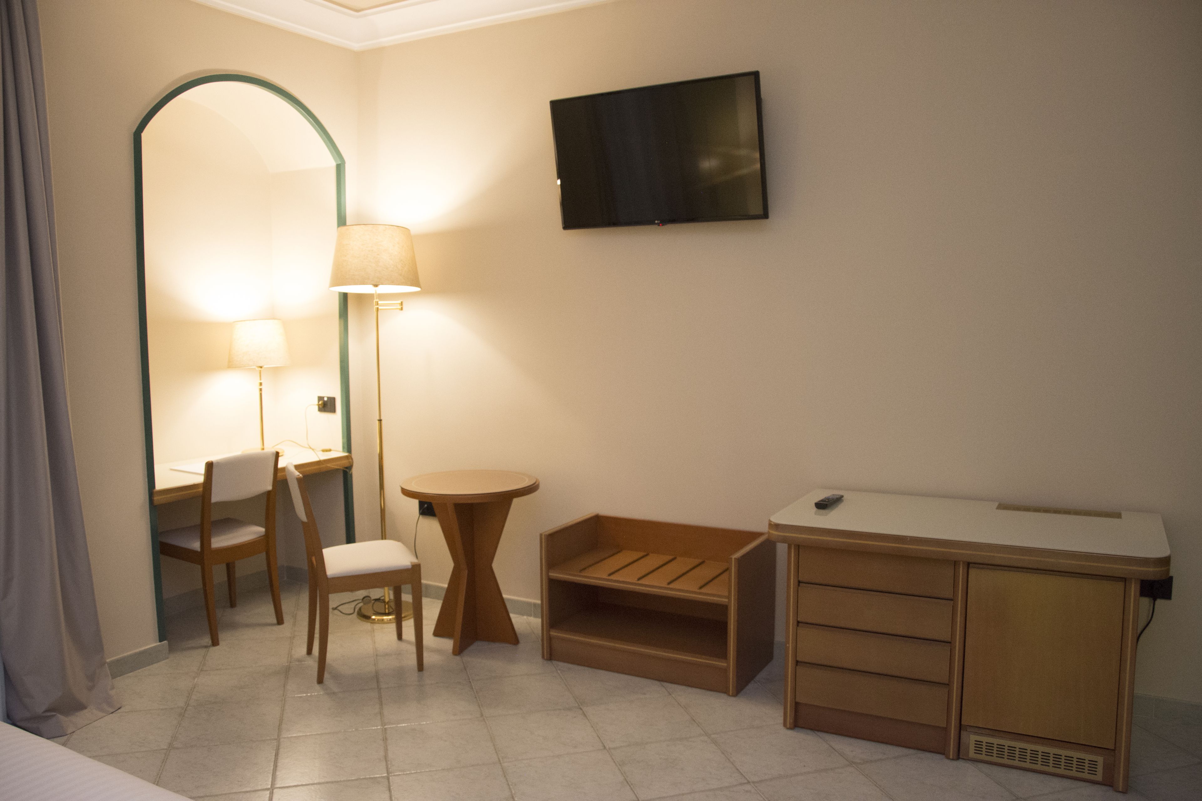Habitación de hotel con escritorio, silla, lámpara, televisión y un pequeño armario de madera.