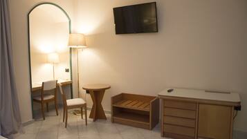 Habitación de hotel con escritorio, silla, lámpara, televisión y un pequeño armario de madera.