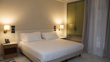 Een net opgemaakt bed in een hotelkamer met twee nachtkastjes, elk met een lamp en een telefoon.