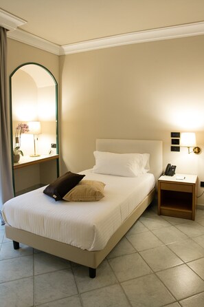 A neatly made bed with white linens and two pillows, a bedside table with a lamp, a phone, and a wall-mounted light fixture. - Hotel Commercio (Battipaglia)
