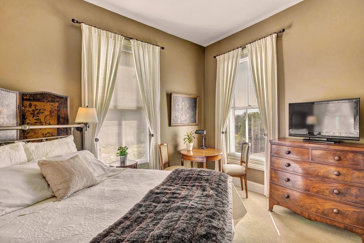 Een slaapkamer met een bed, een dressoir, een televisie en een klein tafeltje met een stoel.