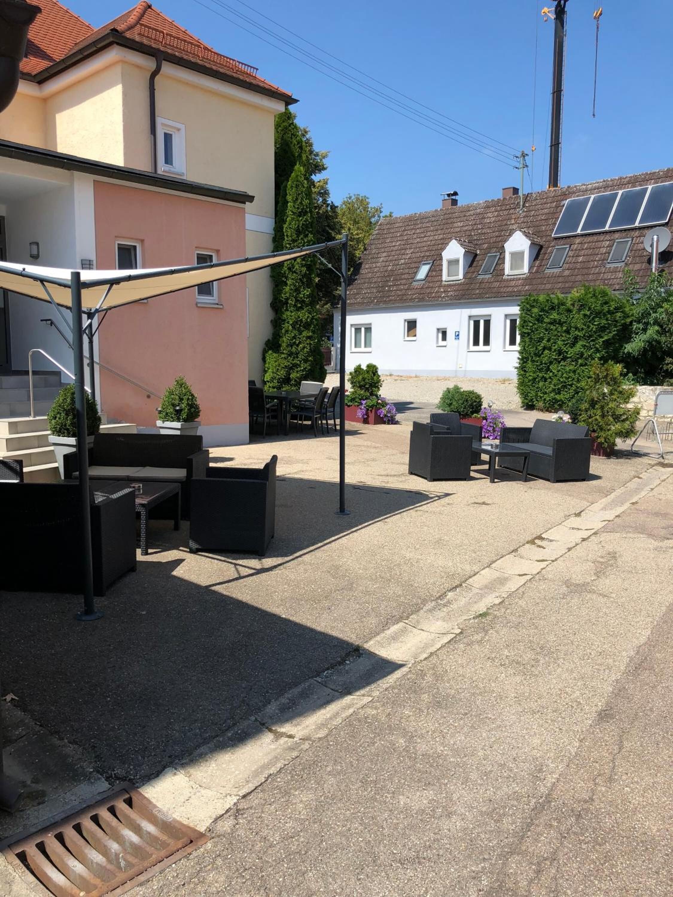 Ett utomhusområde med bord och stolar, ett takförsett sittområde och en byggnad med ett sluttande tak och solpaneler.
