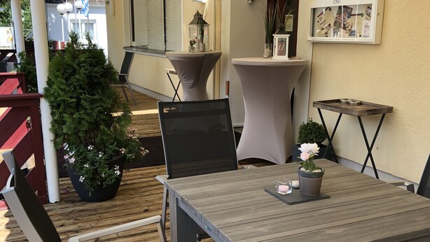 An outdoor patio area with a wooden table and chairs, surrounded by potted plants and a white umbrella. - Hotel Donau (Donauwoerth)