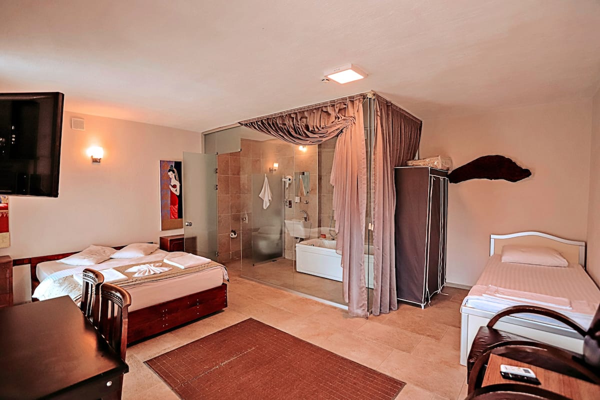 A hotel room with a bed, a desk, a chair, a shower area, and a bathroom.