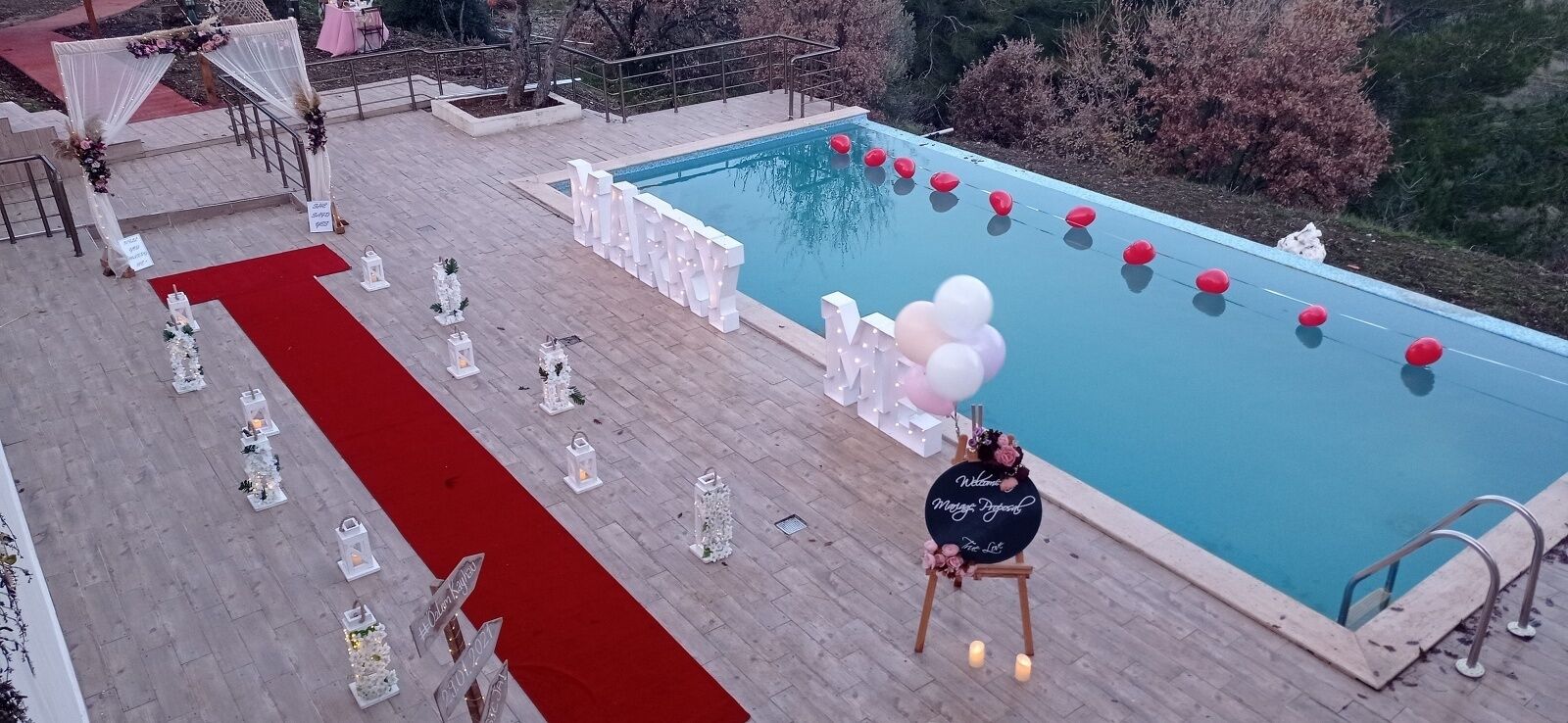 A poolside area with a red carpet, white floral arrangements, and a welcome sign by the pool.