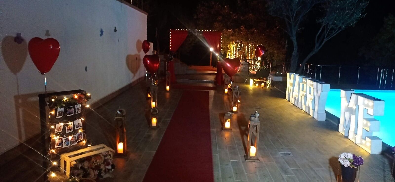 A decorated indoor area with a red carpet, heart-shaped balloons, lanterns, and a backdrop with illuminated letters.