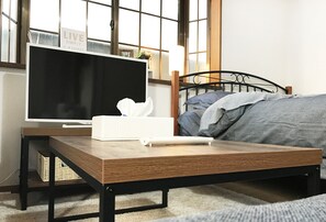 Een slaapkamer met een bed, een nachtkastje met een televisie, een afstandsbediening en een zakdoosje.